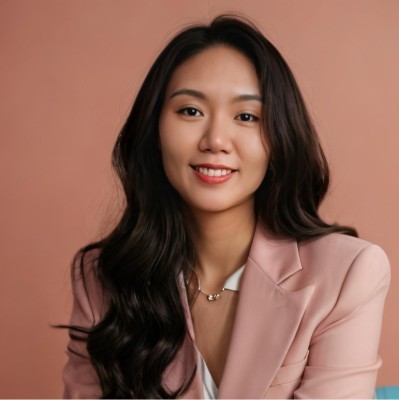 Jewel (Hsiao-Tung) Lo headshot in beautiful peach jacket, silver necklace, long hair to one side smiling with a darker peach solid color background
