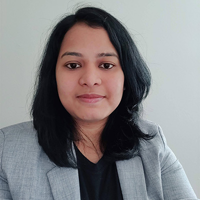 Priyanka Thakur headshot, in grey business jacket, black top with below the shoulder length hair with a slight smile