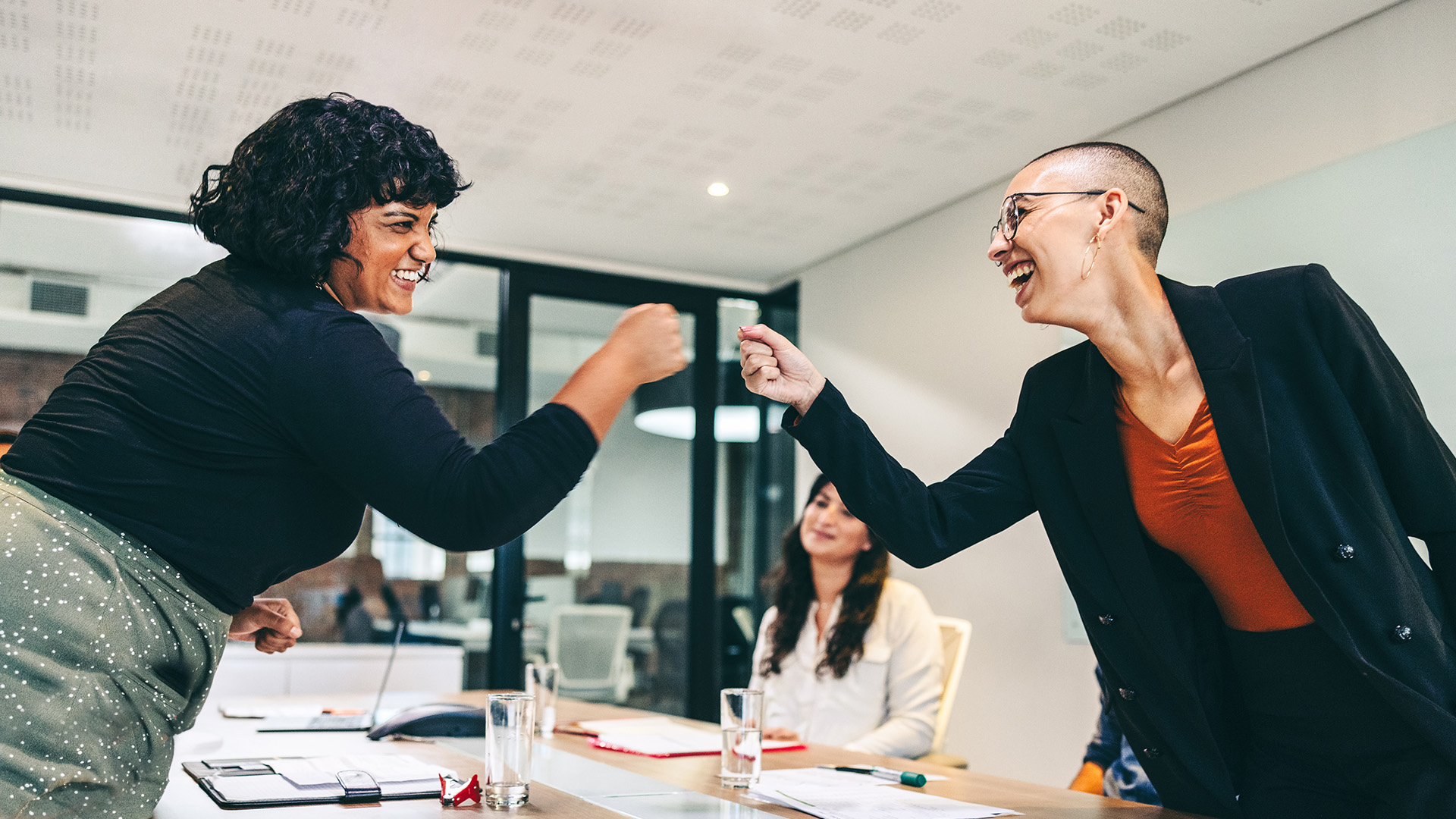 woman tech leader fist bumping another woman that she actively sponsored in a conference room after the meeting
