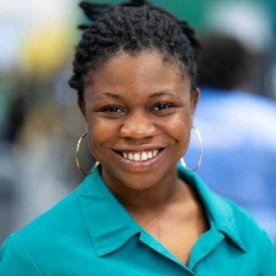 Onyinyechi Nmecha professional headshot wearing a green blouse, gold earrings and smiling brightly